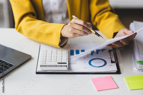 Serious female accountant working with financial documents in office and auditing accounts. Auditor checking financial report documents on desk.
