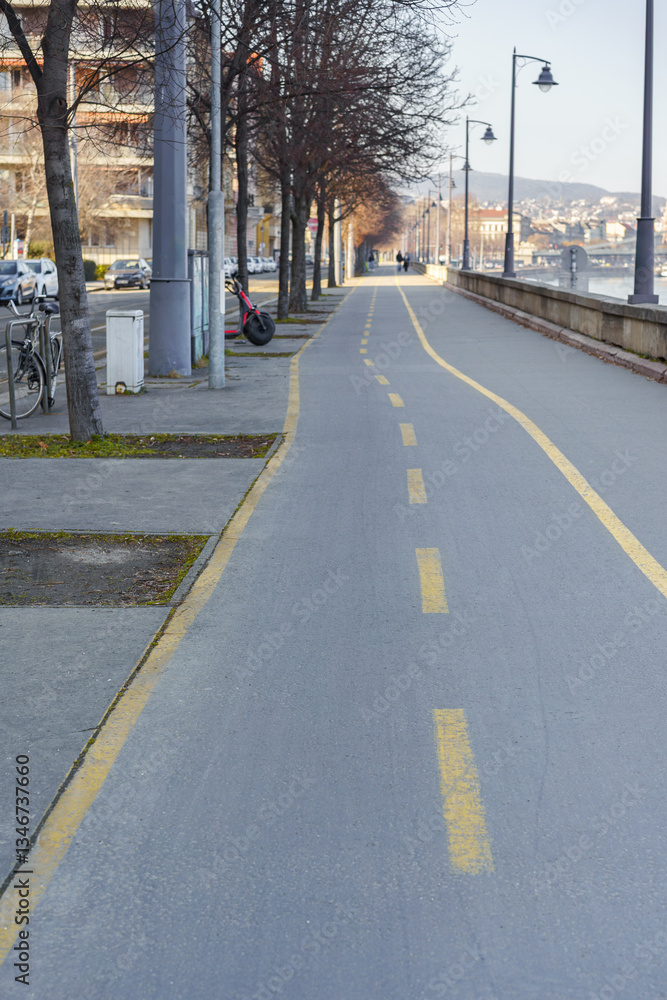 A bicycle lane marked with a yellow line runs along the sidewalk by the riverbank. A bicycle lane marked with a yellow line runs along the sidewalk by the riverbank.