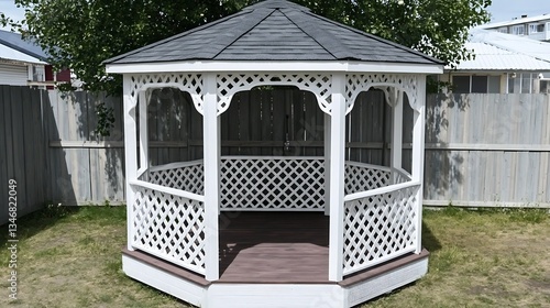 A white gazebo in a backyard with decorative lattice and a fence