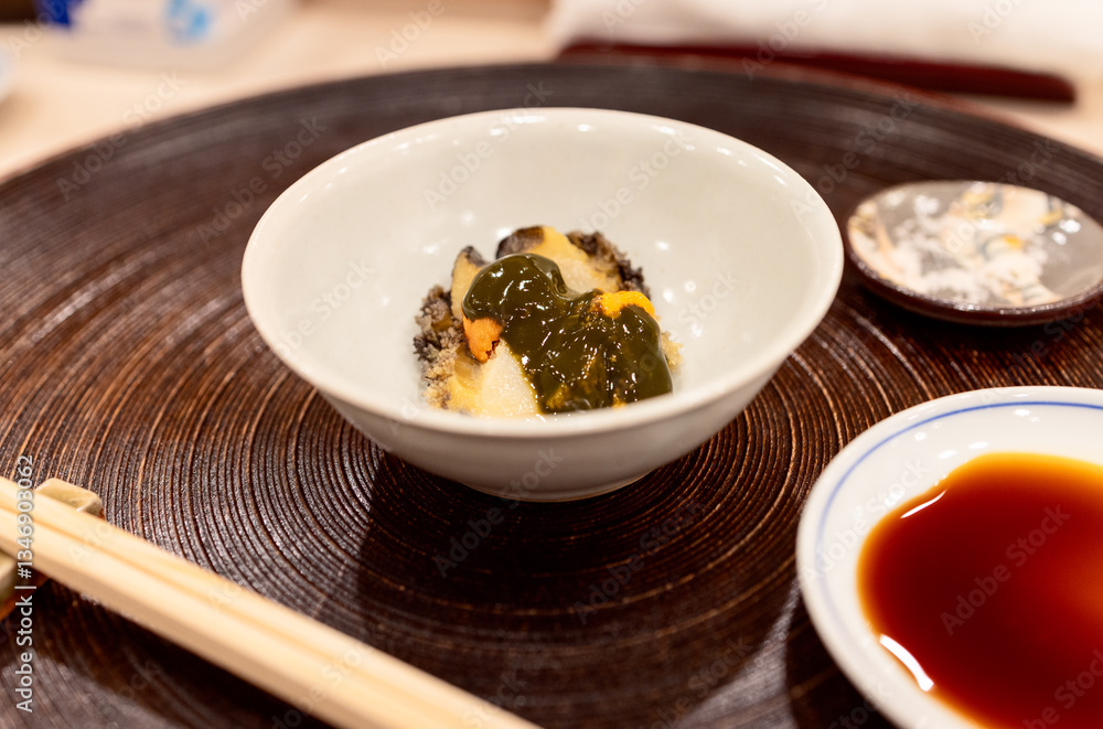 Abalone sashimi topped with sea urchin, elegantly served in a ceramic bowl with soy sauce on the side Abalone sashimi topped with sea urchin, elegantly served in a ceramic bowl with soy sauce on the side