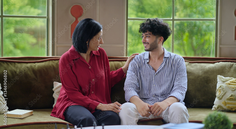 © Raushan_films - Indian happy mature woman lady with young man male sitting on cozy sofa couch talk gossip share story indoor home adult mom teen son boy speak funny joke enjoy day spend time have fun joy inside house
