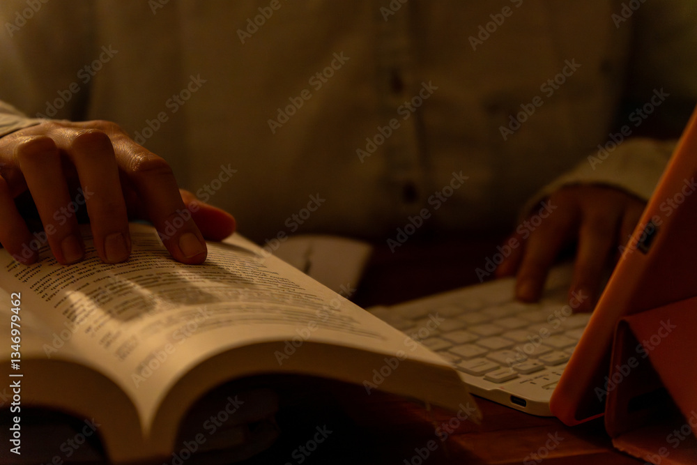 Naklejka premium A student studying at night, typing on a keyboard with books open in front of them