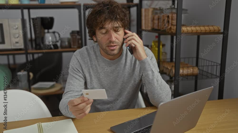 Man talking on phone holding card in home office setting surrounded by shelves displaying kitchen items indicating remote work. Man talking on phone holding card in home office setting surrounded by shelves displaying kitchen items indicating remote work.