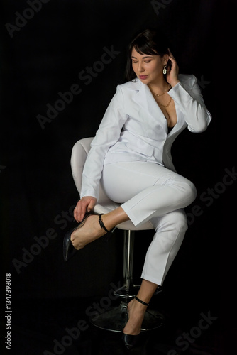 Obraz na płótnie Young pretty woman in a black bra and a business white suit sits on a chair at a black background w salonie
