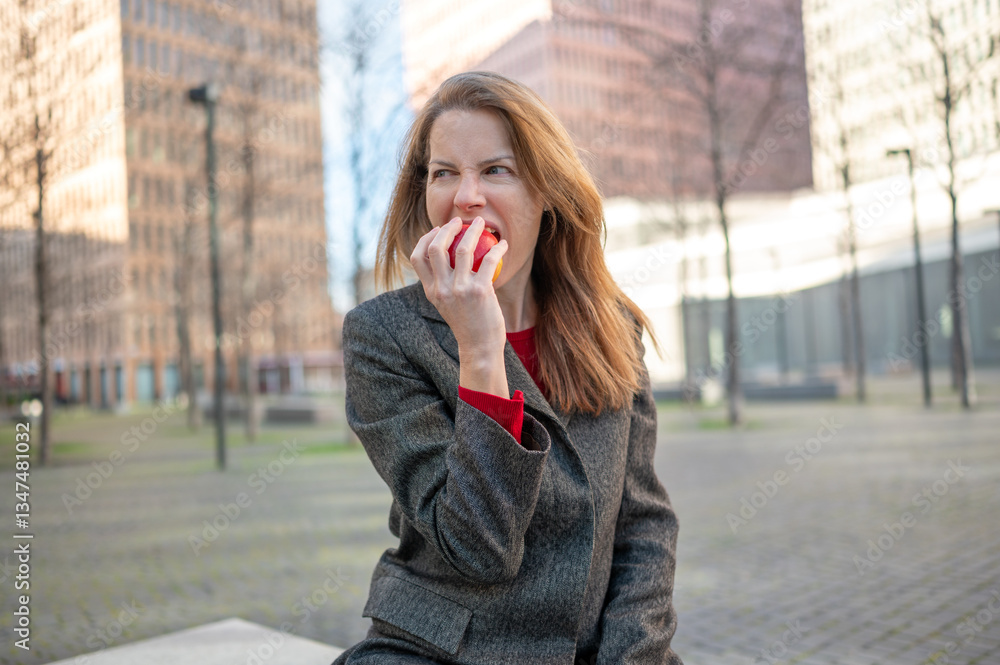 Fototapeta premium Businesswoman aggressively biting into an apple in urban setting
