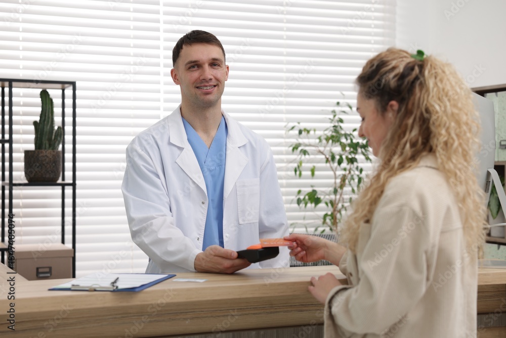 Smiling receptionist taking payment from patient via terminal in clinic Smiling receptionist taking payment from patient via terminal in clinic