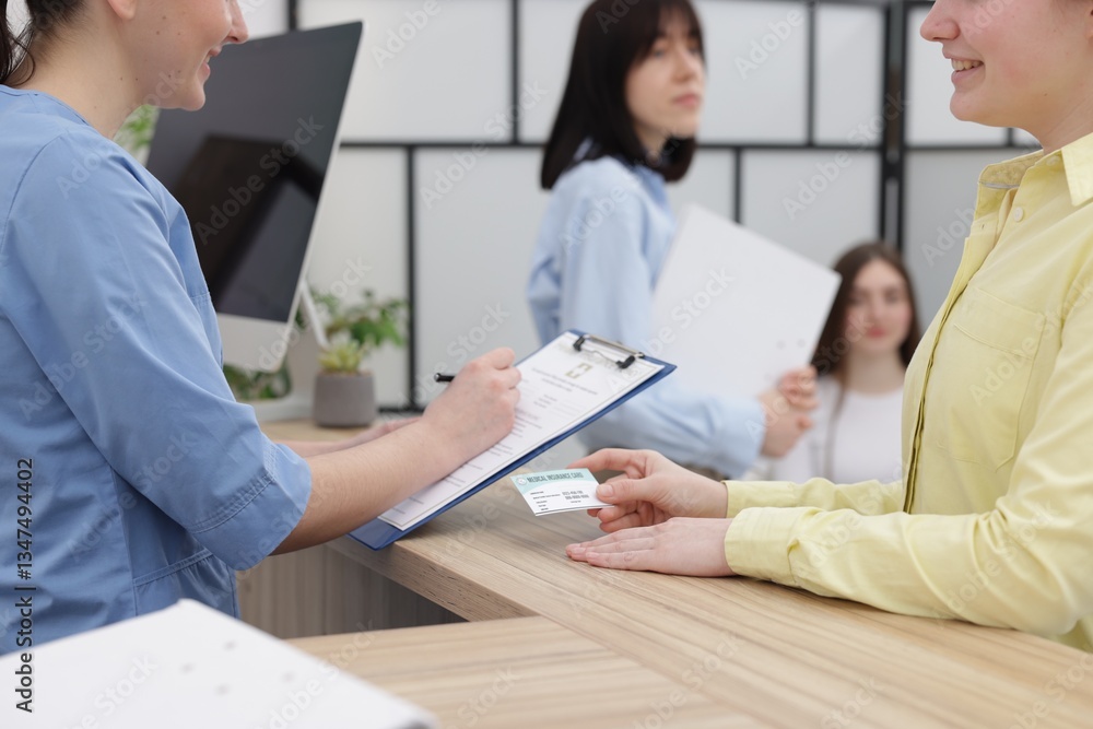 Obraz premium Patient with medical insurance card and receptionist filling document at wooden counter in clinic, closeup