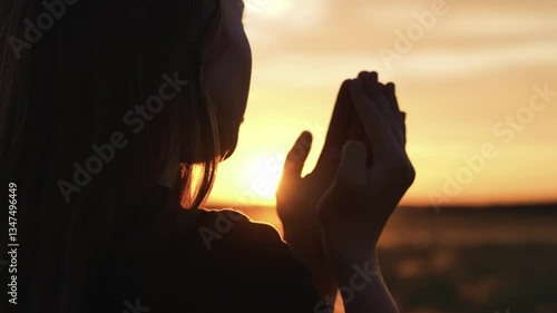Woman praying with folded hands at sunset silhouette. Religious pious orthodox christian spiritual believing faithful girl at morning dawn sunrise reading prayer bible turning to god jesus christ.
