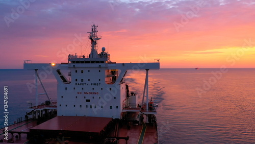 Bulk carrier loaded with grains underway under a crimson sky. Merchant ship Fakarava designed to transport coal, sand or timber. Elegant red ship gliding gently against sun on Black Sea