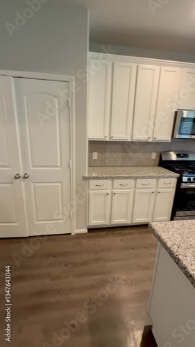 Empty american house kitchen with white cabinets granite countertops wood floors and stainless steel appliances in open concept design. 