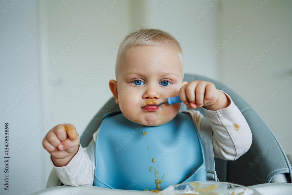 A cheerful and happy baby is joyfully enjoying mealtime while wearing a blue bib and holding a spoon, all set in a bright, minimalist environment that promotes an engaging dining experience