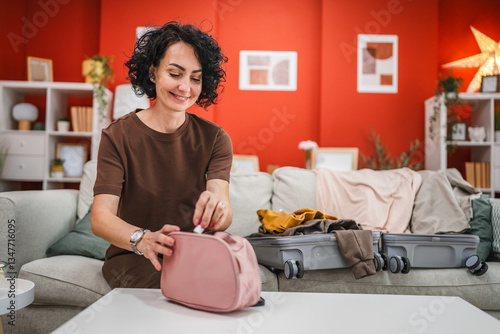 Φωτογραφία curly hair woman sit on sofa and pack cosmetics in a toiletry bag