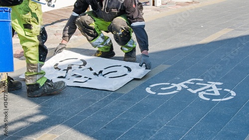 Workers in paint-stained overalls renew the marking of the bicycle path in the spring with the help of a stencil and a spray bottle