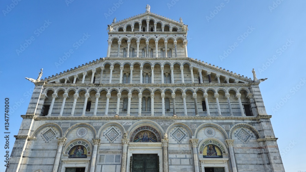 Fototapeta premium December 30, 2024: The ornate facade of the Pisa Cathedral in Italy, featuring white marble, intricate arches, columns, and religious mosaics under a clear blue sky.