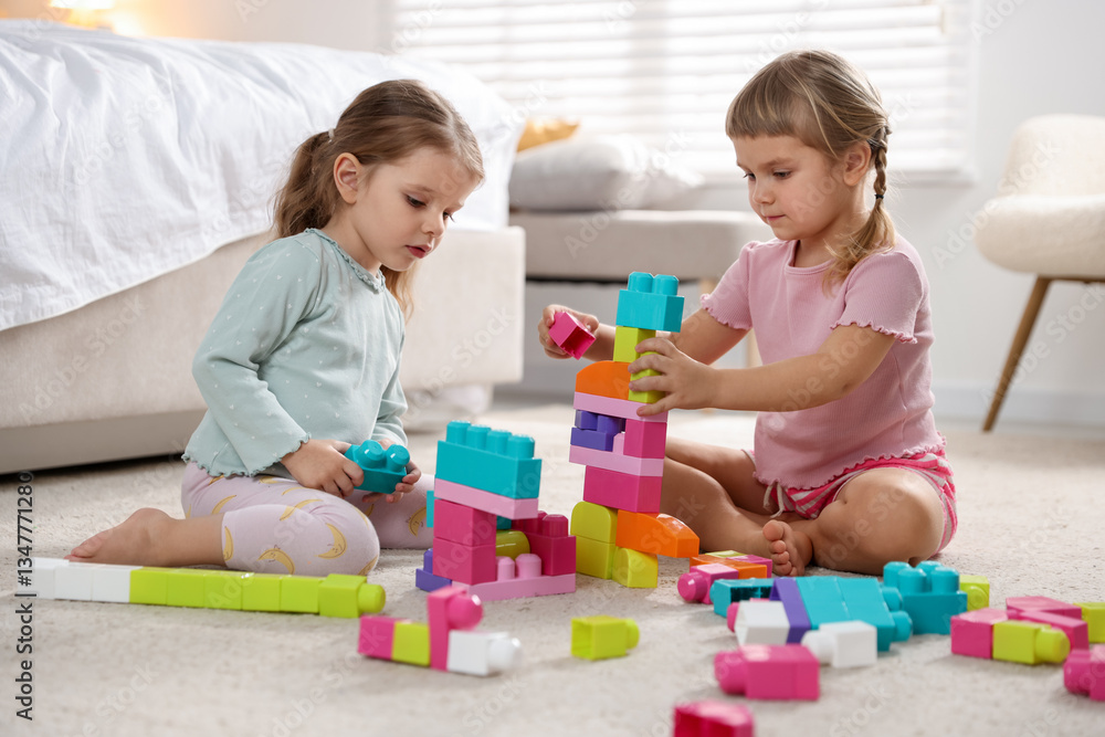 Cute little sisters playing with colorful building blocks on floor at home Cute little sisters playing with colorful building blocks on floor at home