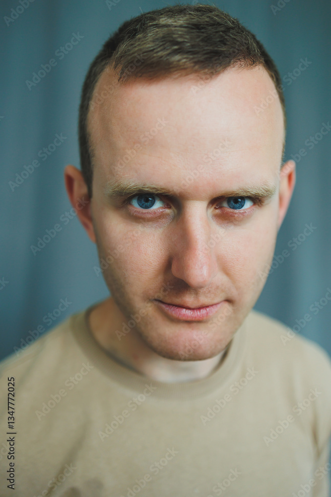 Obraz premium An Intense and Compelling Portrait of a Young Man Featuring Strikingly Blue Eyes and CloseCropped Hair Set Against a Soft and Subtle Background Enhancing His Charismatic Presence and Style