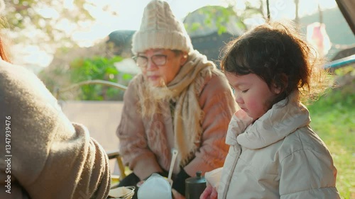A candid moment of an elderly Asian woman and a grandchild girl enjoying breakfast morning outdoors. warmly dressed in cozy winter clothing with sunlight creating a serene, intimate family scene.