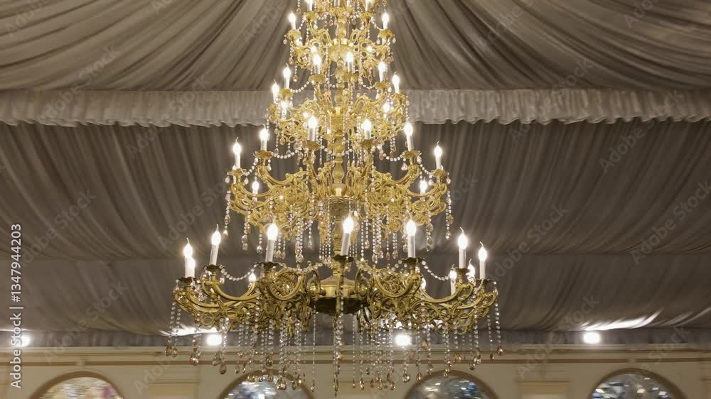 A grand marquee adorned with luxurious chandeliers and draped ceilings. A smooth drone movement captures the elegant wedding or event hall ambiance with warm lighting and intricate details. A grand marquee adorned with luxurious chandeliers and draped ceilings. A smooth drone movement captures the elegant wedding or event hall ambiance with warm lighting and intricate details.