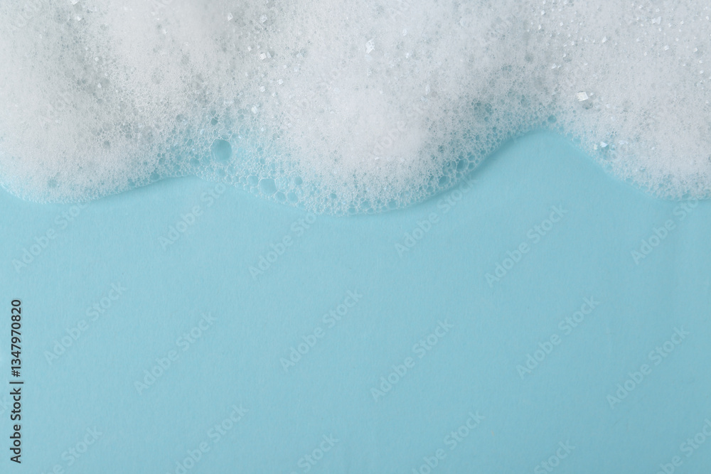 Fototapeta premium White fluffy foam on light blue background, top view. Space for text
