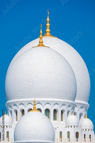 Close-up of the Sheikh Zayed Grand Mosque, showcasing its intricate white marble domes and elegant architectural details against a vivid blue sky. 
