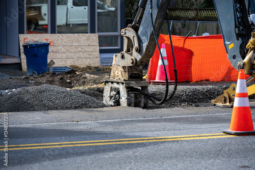 Roadworks covering trench dug for underground utilities with gravel and compacting with vibrating tamper attachment on excavator machine, new housing development construction project
