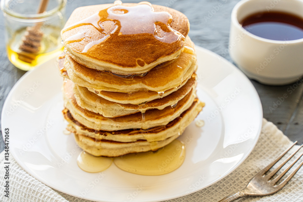 Pancakes poured with honey on a white plate with napkin and coffee on a gray background Pancakes poured with honey on a white plate with napkin and coffee on a gray background