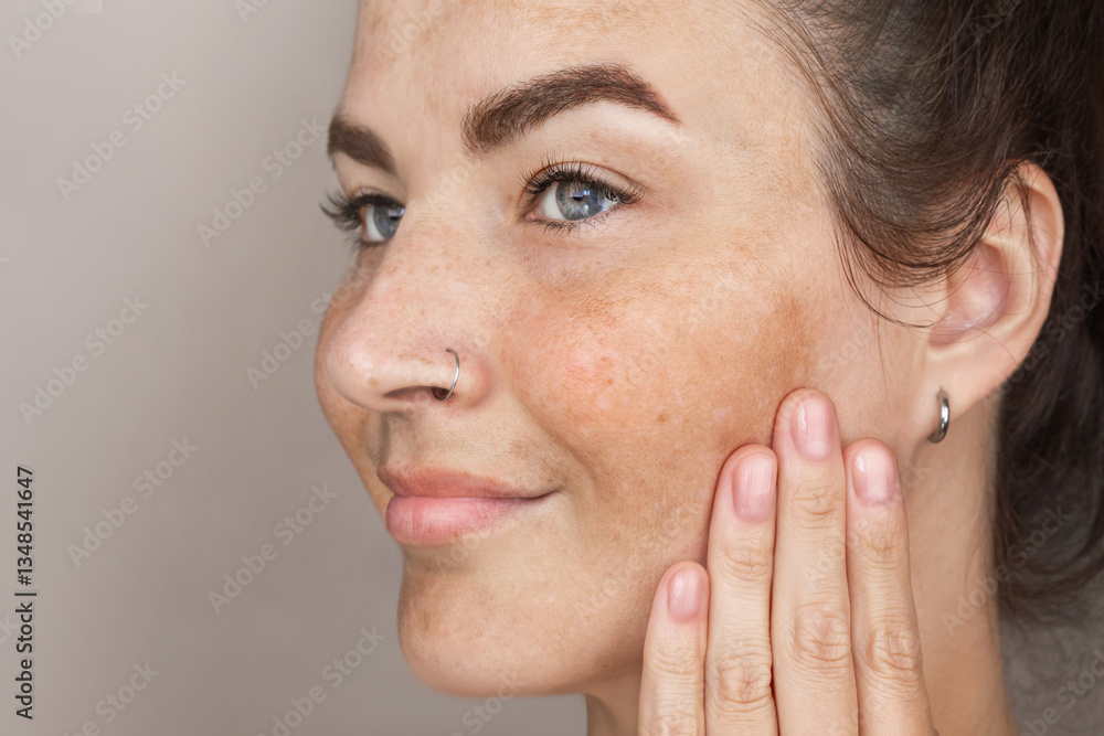 Fototapeta premium Portrait of cropped caucasian middle aged woman face with freckles touching skin by hand. Age spots on the face, melasma. Woman with blue eyes