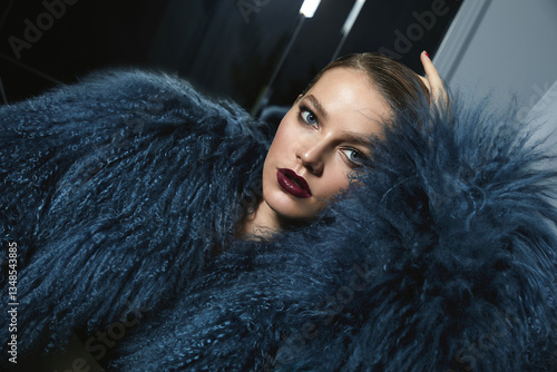 Portrait of a beautiful young woman in a blue fashionable studio fur coat and with bright evening make-up. Smooth hairstyle, combed hair. Advertising of fashion and beauty. Decorative cosmetics.