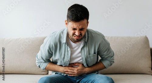Young man with stomach pain sitting on couch, wincing