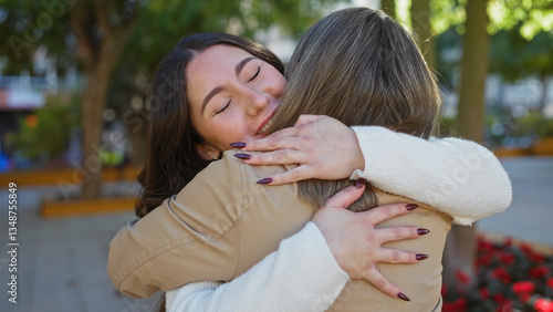 Photos Woman hugging daughter in urban park setting, displaying love and warmth in an outdoor city environment