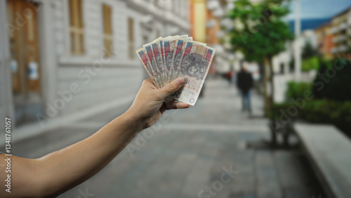 Man holding polish zloty banknotes in hand, standing on a city street outdoors, highlighting money in an urban setting.