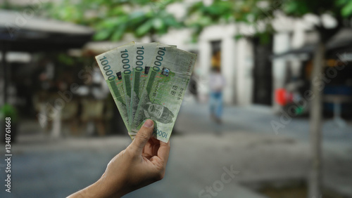 Street view shows man holding south korean won banknotes in hand with cityscape background, capturing an urban financial transaction in a bustling outdoor environment.