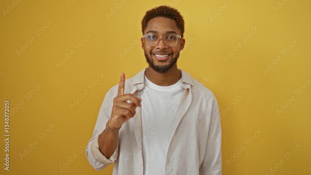 Handsome young man smiling over an isolated yellow background, pointing with one finger up, signaling number one with a confident expression Handsome young man smiling over an isolated yellow background, pointing with one finger up, signaling number one with a confident expression