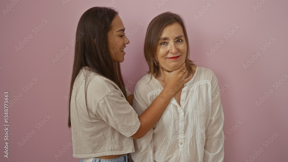 Woman smiling while daughter playfully holds her neck against a pink wall, symbolizing family love and friendship between two women. Woman smiling while daughter playfully holds her neck against a pink wall, symbolizing family love and friendship between two women.