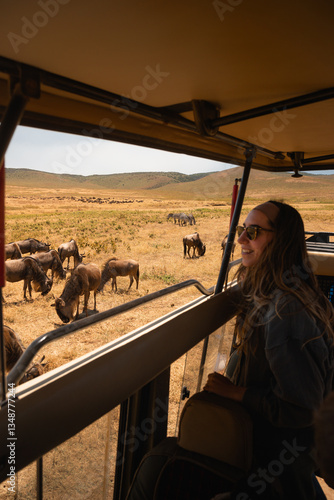 Young woman enjoying a safari trip, observing wildebeest grazing in the picturesque landscape of ngorongoro crater, tanzania
