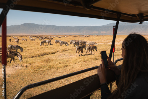 Tourist taking pictures of zebras grazing in the ngorongoro crater, tanzania, during an african safari
