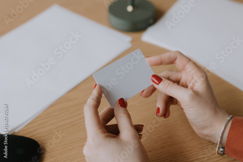 Person holds a blank card while seated at a wooden table surrounded by stationery in a cozy indoor setting