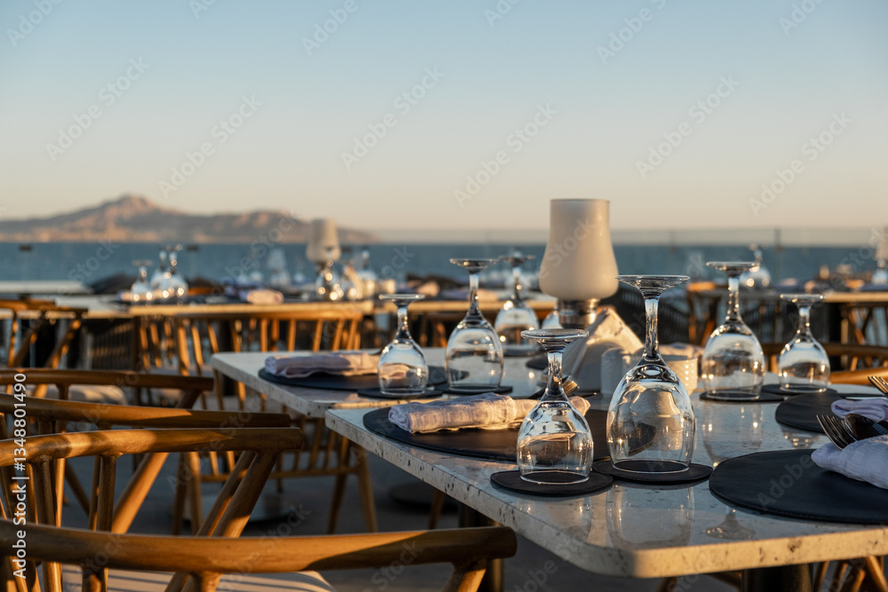 Fototapeta premium Perfectly arranged restaurant tables by the ocean, with fine glassware