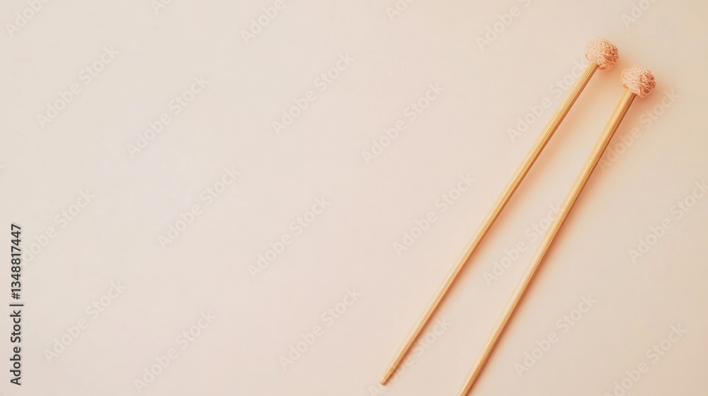 A pair of light-beige mallets rest on a pale pink background. Simple, minimalist aesthetic. A pair of light-beige mallets rest on a pale pink background. Simple, minimalist aesthetic.