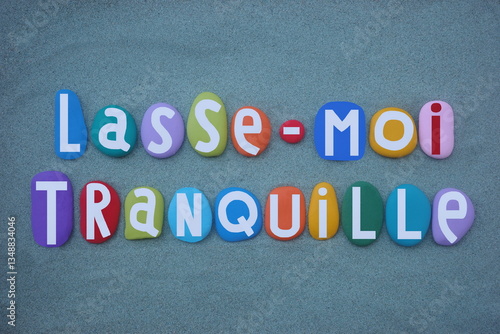 Lasse-moi tranquille, french phrase meaning leave me alone, creative text composed with multi colored hand painted stone letters over green sand