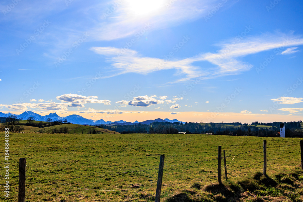 Obraz premium Alpine landscape with green meadows, snow-capped mountains and Saharan dust glow at sunset, Bavaria, Germany, 21.3.2025