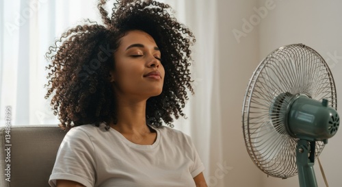 Woman relaxing in a chair, enjoying the cool breeze from a fan, creating a calm and peaceful atmosphere.
