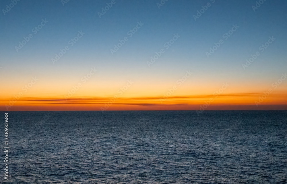 Fototapeta premium Beautiful orange sunset or sunrise over ocean, calm water. Vibrant colors, horizontal. Clear sky with a few wispy clouds. Copy Space.