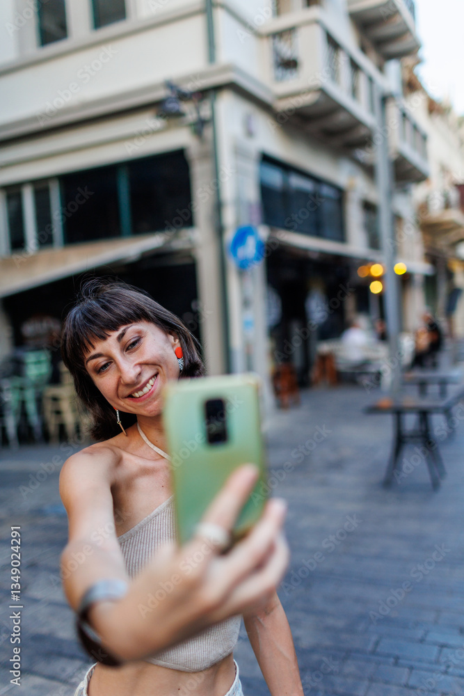 Fototapeta premium Young woman walks the streets and takes selfie using smartphone camera. Beautiful young photographer takes pictures for her travel blog.