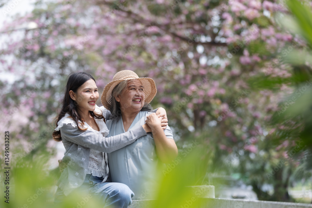 Naklejka premium A loving daughter embraces her mother, both smiling under blooming cherry blossoms. 