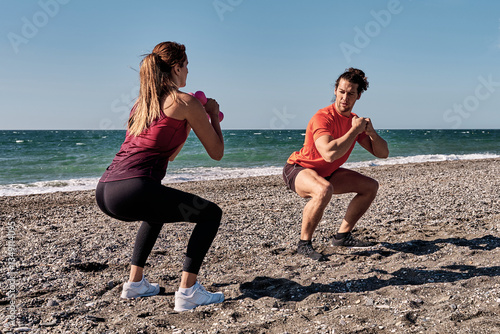 Personal trainers performing squats on the beach during summer vacation