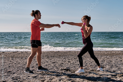 Personal trainer guiding woman exercising with dumbbells on beach