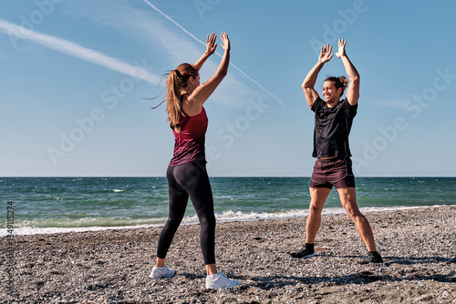 Personal trainers performing jumping jacks on the beach