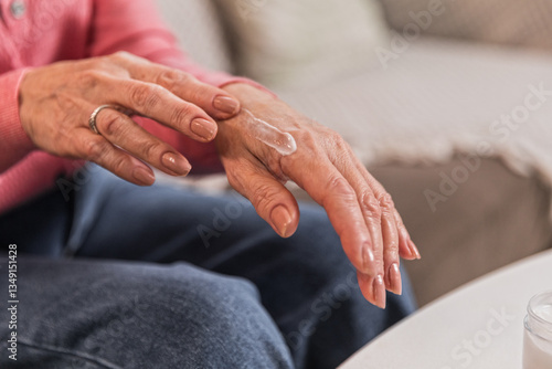 Senior woman in 60s nourishing hand cream to skin, taking care of hands.
