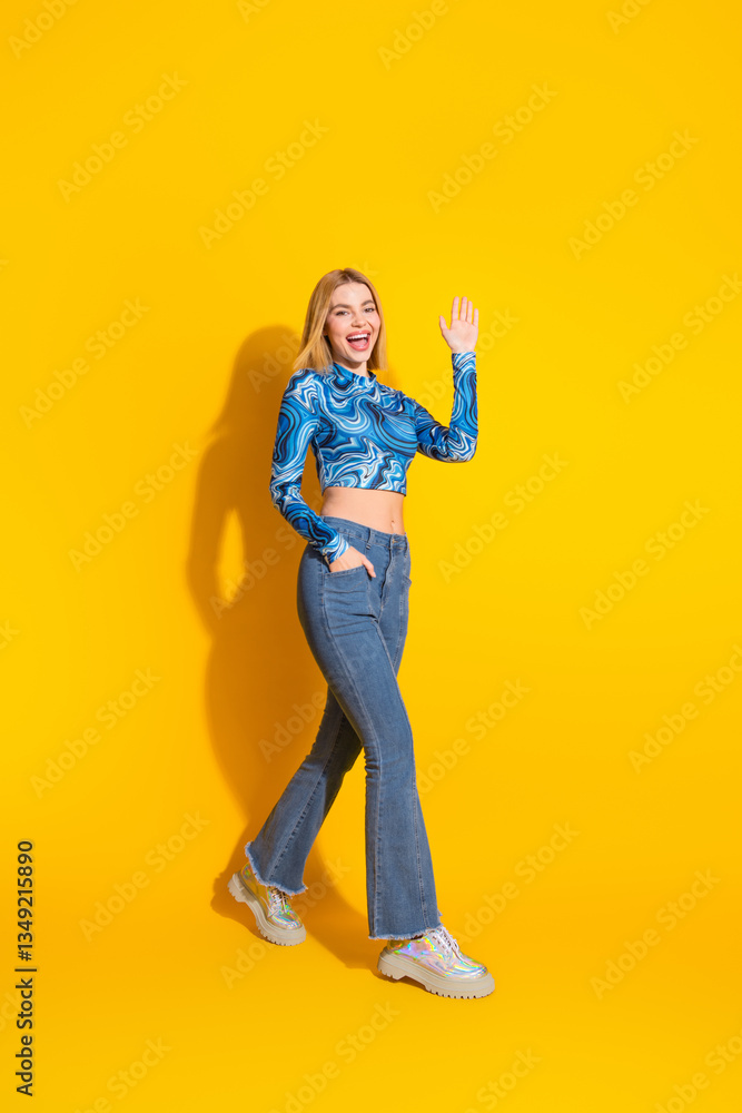 Young woman waving in a stylish casual outfit with a vibrant yellow vertical background Young woman waving in a stylish casual outfit with a vibrant yellow vertical background